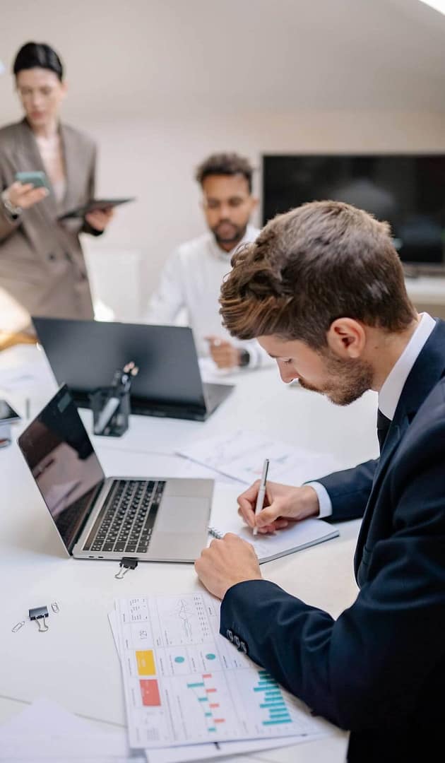 Team meeting in an office with a laptop, notes, and printed charts on the table